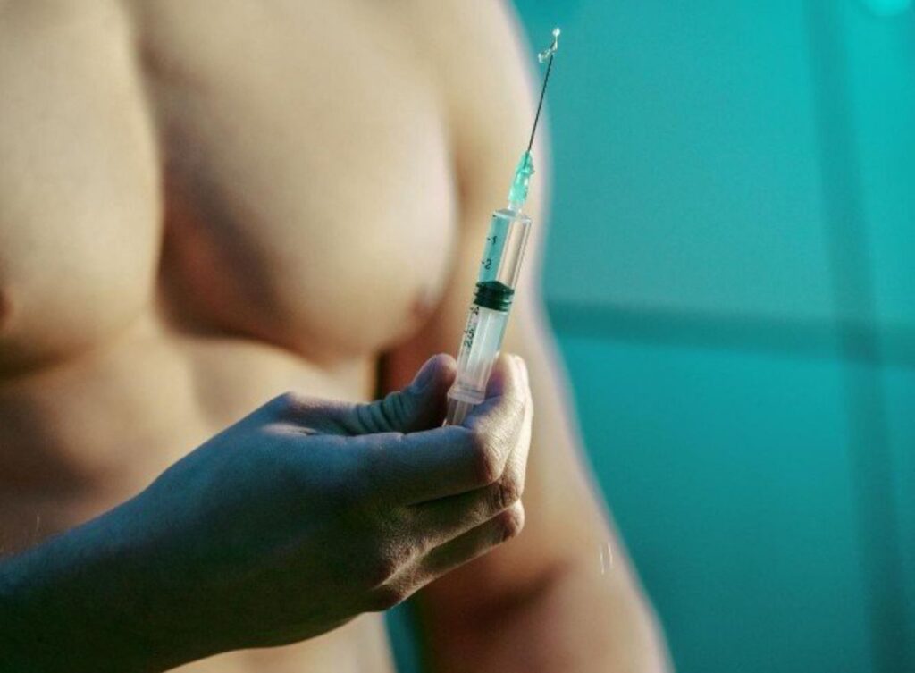 A shirtless man holding a syringe filled with a liquid, possibly testosterone, preparing for an injection.