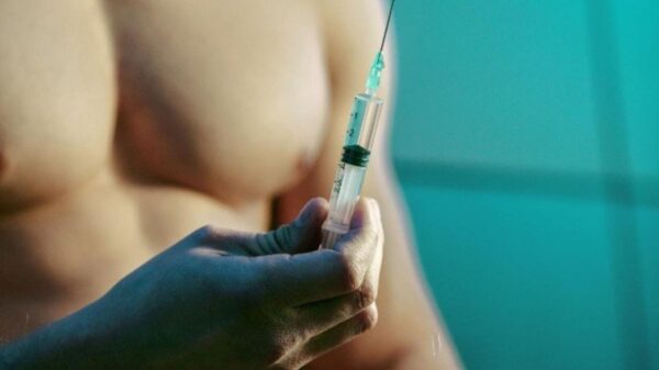 A shirtless man holding a syringe filled with a liquid, possibly testosterone, preparing for an injection.